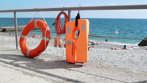 Orange life jacket and lifebuoy on beach by sea. Safety equipment for rescuing people on seashore.