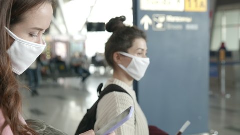 People in protective mask staying in a queue for boarding on plane. Two women in airport terminal waiting checkpoint prevent themselves from coronavirus. Pandemic covid-19 concept.