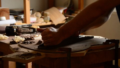 Luthier manufacturing a guitar in the workplace with a wood planer