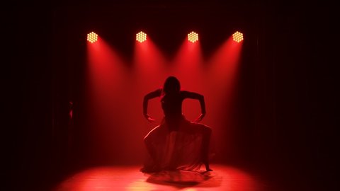 Young elegant female dancer in black costume performing contemp choreography in the smoke of a dance studio. Silhouette. Slow motion.