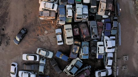 Aerial top view of the car dump with hundreds of cars stacked waiting to be recycled. A lot of unecological, harmful, old, wrecked cars are standing on the junkyard.
