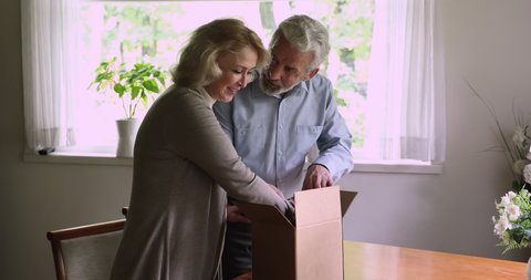Middle-aged couple made order on internet online shop received items package open parcel feels satisfied by qualified goods from internet, got present form friends. Quick safe delivery service concept