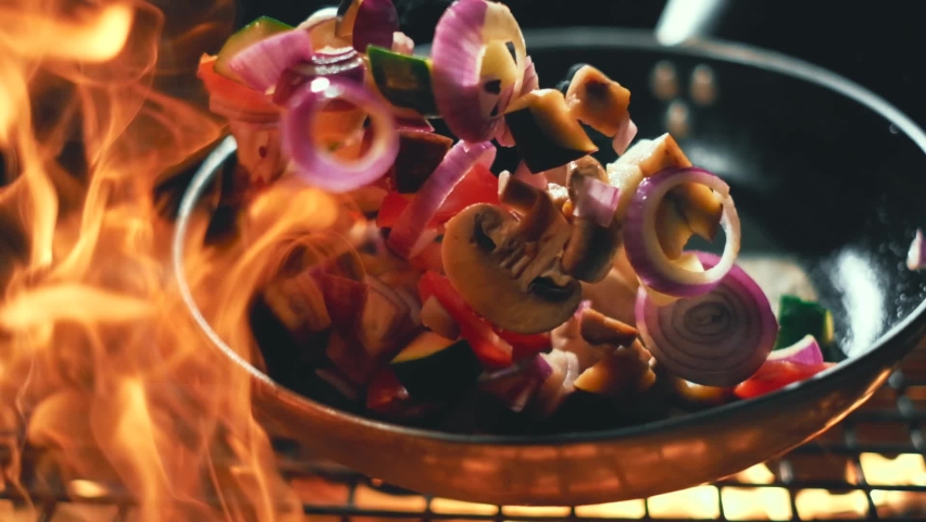 Vegetables flying into the pan in slow motion. Onions, broccoli, mushrooms, champignons, tomatoes, zucchini. Healthy vegetarian food. Cooking on fire | Shutterstock HD Video #1060959961