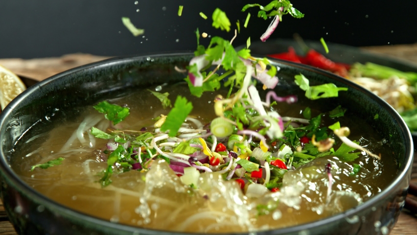 Super Slow Motion Detail Shot of Ingredients Falling into Vegetable Pho Soup at 1000 fps.