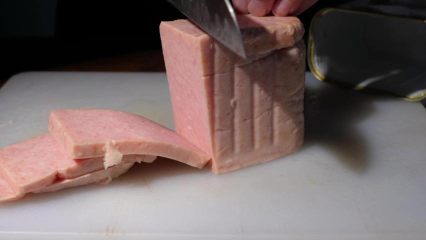 This close up video shows anonymous hands cutting and slicing a block of canned ham on a cutting board with a kitchen knife.  Royalty-Free Stock Footage #1060960285