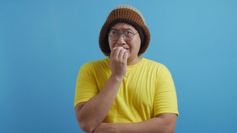 Portrait of young funny nervous Asian man biting his nails as if he is worried afraid of something bad