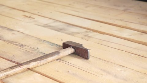 hands driving a nail with a hammer into a wooden board in natural light