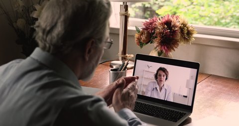 Laptop screen view over old 50s male shoulder during talk with medical worker, patient asks female doctor, receive medical aid online due quarantine coronavirus pandemic outbreak, telemedicine concept