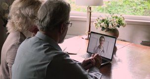 Rear view aged couple having online consultation with doctor by video call, pc screen over spouses shoulder. General practitioner consults gives advice to older people remotely use modern tech concept