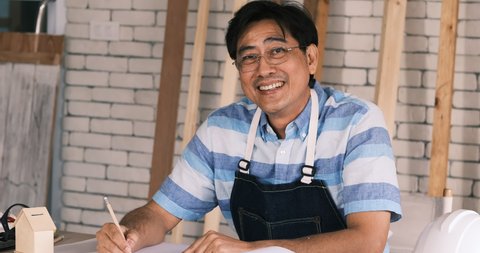 Portrait of middle age carpenter sit with sketch blue print on work table  and smiling to camera.