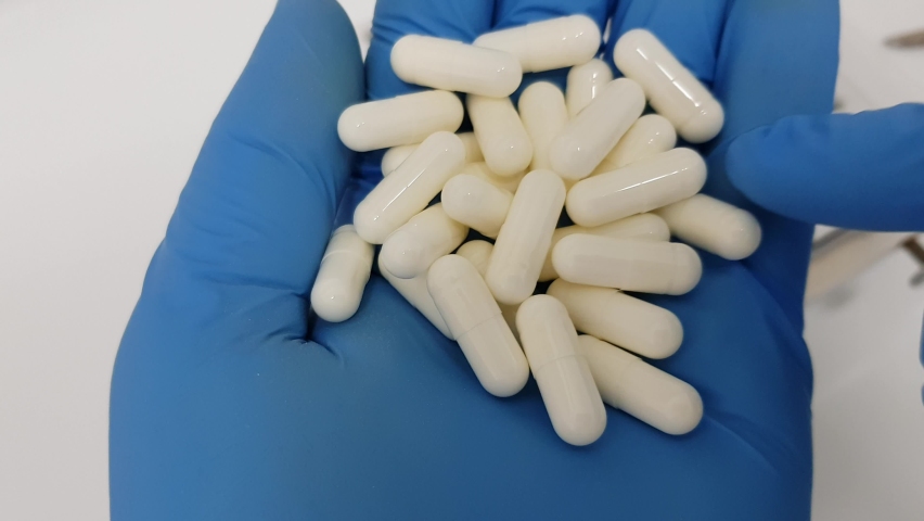 Lab pharmacist inspects white pill capsules. Close up