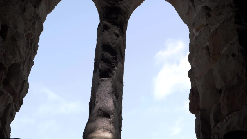 Arched windows on old building ruins against blue sky tilting shot