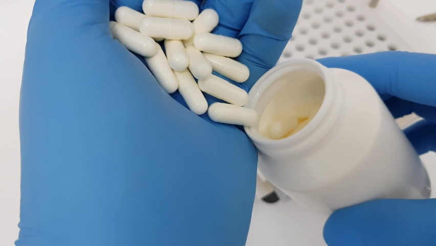Inspection of white pill capsules. Lab technician fill bottle.