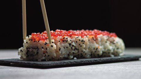 Sticks Take Sushi from Sushi box. Variety of types sushi with red caviar, fish, Philadelphia cheese and chopsticks close-up. Set of delicious Japanese sushi rolls on a stone board on a black