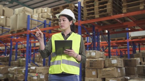 beautiful asian japanese woman manager working on tablet to check stock entering information in warehouse.