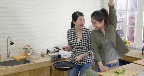 slow movement of two asian korean girl friends having fun in kitchen while cooking healthy meal. and success with flipping pancake on hot pan and show to roommate.