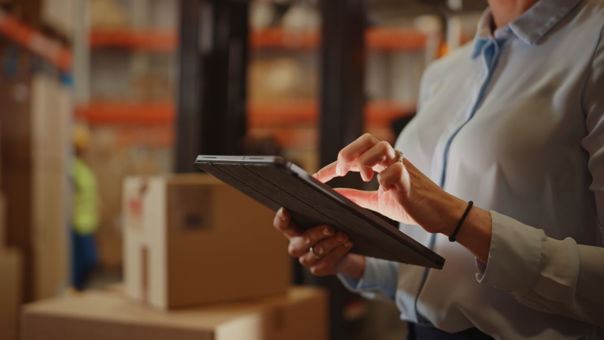 In Warehouse Manager Uses Digital Tablet Does Inventory, Using Touch Screen Gestures, Checking Package Delivery. Distribution Center with Shelves with Cardboard Boxes. Focus on Hands and Device Royalty-Free Stock Footage #1060977100