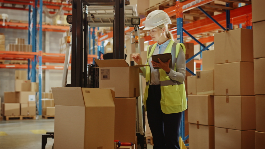 In Warehouse Female Manager Wearing Hardhat Standing beside Forklift Uses Digital Tablet for Inventory, Checking Inside of Cardboard Box Package. Distribution, delivery Center, Shelves with Packages Royalty-Free Stock Footage #1060977103