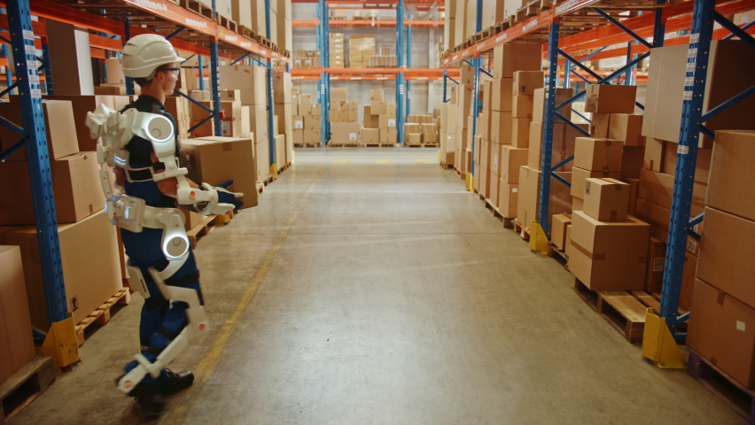 High-Tech Futuristic Warehouse: Worker Wearing Advanced Full Body Powered exoskeleton, Walks with Heavy Cardboard Box. Exosuit amplifies Human Performance, Strenght, Eliminates Work Related Injuries Royalty-Free Stock Footage #1060977157