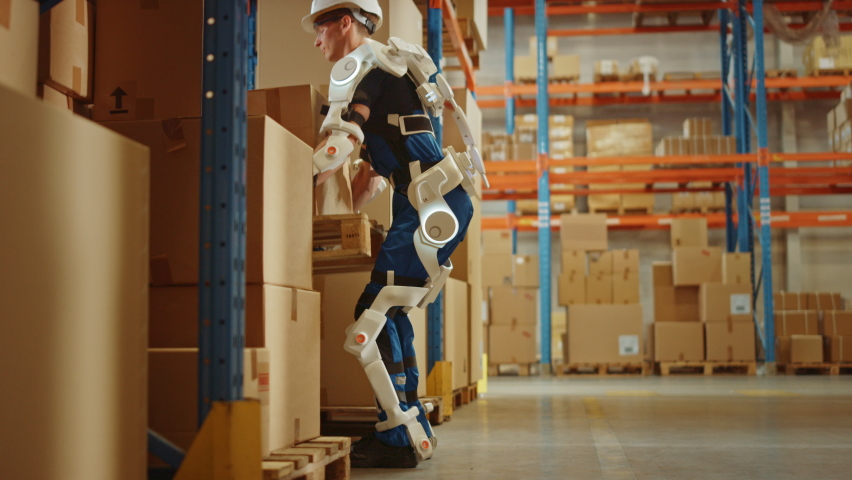 High-Tech Futuristic Warehouse: Worker Wearing Advanced Full Body Powered exoskeleton, Lifts and Walks with Heavy Pallet full of Cardboard Boxes. Delivery Exosuit amplifies Strenght. Following Shot Royalty-Free Stock Footage #1060977169