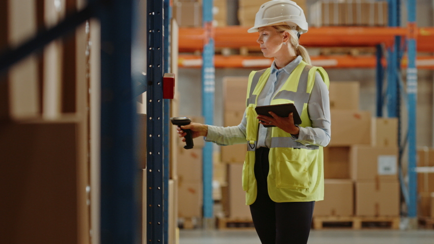 High-Tech Futuristic Warehouse: Manager Scans Packages for Inventory, Delivery in the Background Worker Wearing Advanced Full Body Powered exoskeleton, Walks with Heavy Pallet full of Cardboard Boxes Royalty-Free Stock Footage #1060977181