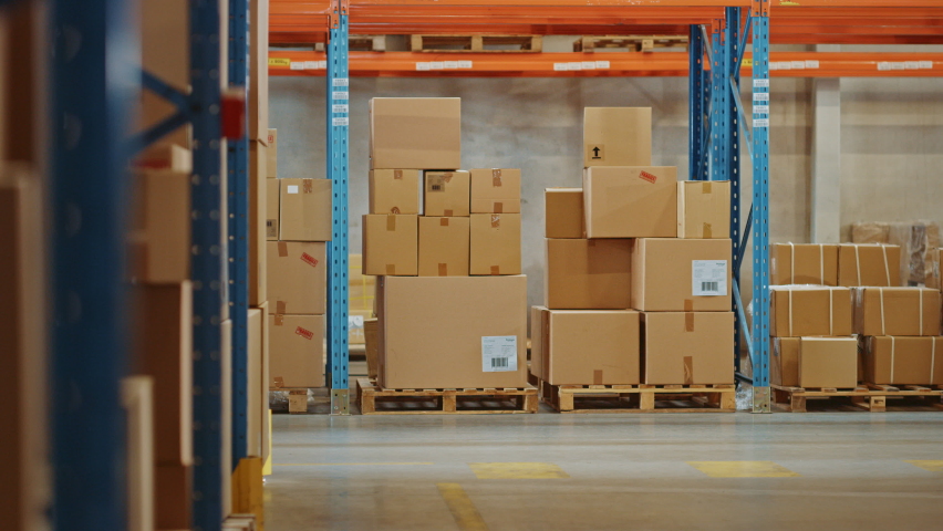 High-Tech Futuristic Warehouse: Manager Scans Packages for Inventory, Delivery in the Background Worker Wearing Advanced Full Body Powered exoskeleton, Walks with Heavy Pallet full of Cardboard Boxes Royalty-Free Stock Footage #1060977184