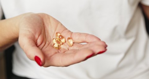 Close up of woman hand holding capsules pills organic vitamins fish oil from meds bottle. Diet nutrition and healthy concept. Vitamin E, A,  Omega 3.