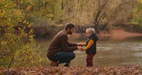 loving father and little son are communicating at nature, on shore of lake at autumn day, man and boy are snuggling by foreheads