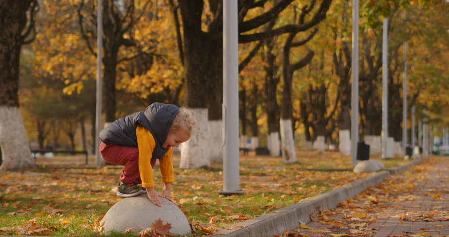 autumn day in park, cute little child is playing, smiling and showing tongue to camera, full length shot at daytime