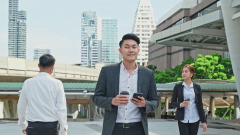 Asian young smart businessman using smartphone in city. The man holding phone walking outdoor to working office with smile face. Telecommunication and mobile network for business concept