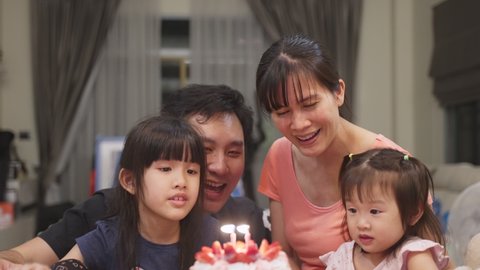 Lovely enjoy moment, Asian young family having birthday party for young little child together at home. Parents hugging her kids and sing happy birthday song then blow air to the candles with happiness