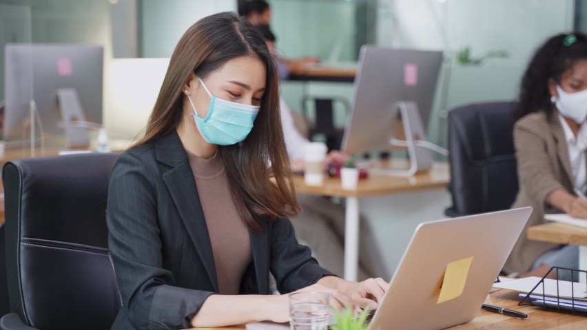 Asian young businesswoman working on computer in office with new normal lifestyle concept. Man and woman wear protective face mask and keep distancing to prevent covid virus after company reopen again Royalty-Free Stock Footage #1060980133