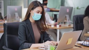 Asian young businesswoman working on computer in office with new normal lifestyle concept. Man and woman wear protective face mask and keep distancing to prevent covid virus after company reopen again - Powered by Shutterstock - Get 15% off with code: PIKWIZARD15