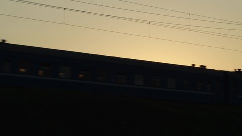 Passenger train with compartments of corridor coaches rides on the railway at sunset in silhouette. Railroad carriage wagons going in daytime. Travel and tourism.