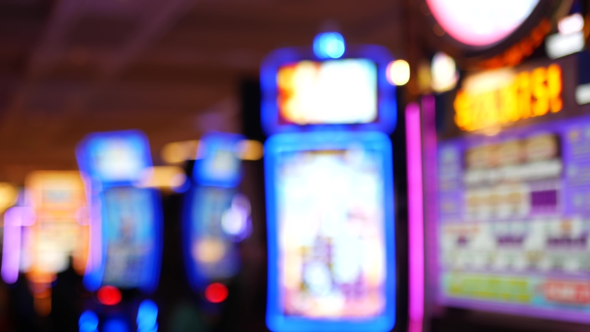 Defocused slot machines glow in casino on fabulous Las Vegas Strip, USA. Blurred gambling jackpot slots in hotel near Fremont street. Illuminated neon fruit machine for risk money playing and betting. | Shutterstock HD Video #1060982026