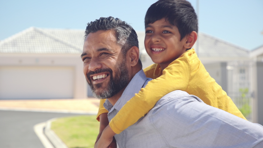 Happy indian father giving piggyback ride to his son and looking at camera. Cute ethnic boy with dad playing outdoor. Close up face of handsome man carrying on shoulders his middle eastern kid. Royalty-Free Stock Footage #1060982695