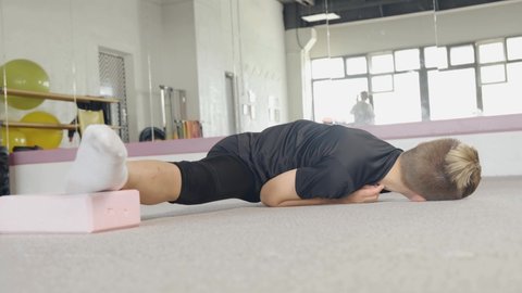 A young guy performs flexibility exercise lying on the floor and help himself with his hands. Flexible, beautiful body. The concept of sports and meditation. Stretching and yoga workout.