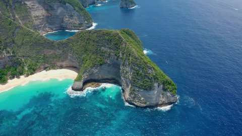 Aerial view of mesmerizing scenic Kelingking Beach with a sheer cliff and a cape covered with dense greenery washed by turquoise sea water on a sunny warm summer day.