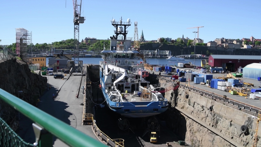 View over the Stockholm harbor island Beckholmen a place for ship repairing. A ship under maintenance in a graving dock and a commuting boat passing on it´s way to the Stockholm archipelago.  
