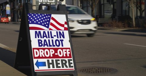 A sign on the sidewalk of a large city shows where to drop off official mail-in ballots.	