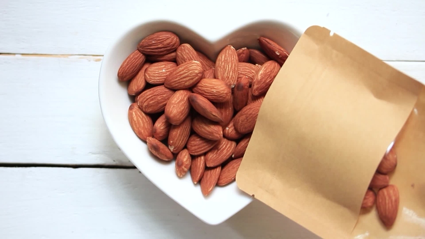 Pour the almonds from the pouch into the heart-shaped plate on a white wooden plate. | Shutterstock HD Video #1060997374