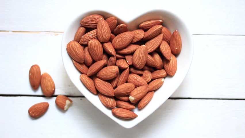 Take the almonds out of a heart-shaped plate. On a white wood scene | Shutterstock HD Video #1060997377