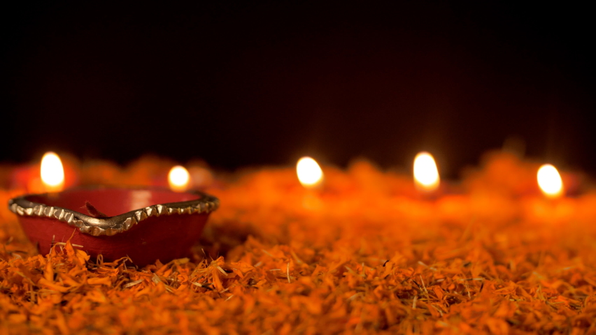 Woman's hand lighting decorative colorful Diyas for Diwali - Hindu festival. Close up shot of colorful Deepavali oil lamps in beautiful formation with flowers in the middle