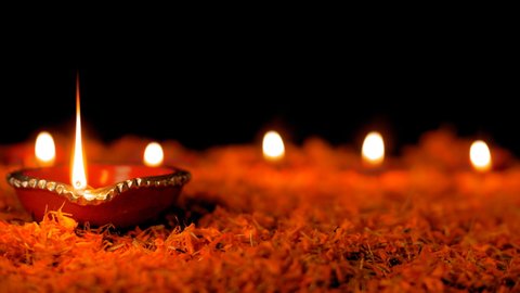 Earthen oil lamps burning on a beautiful flower decoration - Diwali. Closeup shot of decorative floral rangoli with some Puja Diyas lighted with bright flames