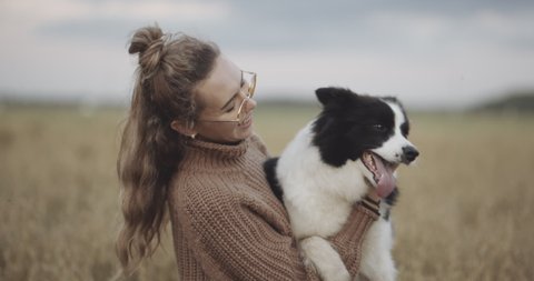 Portrait of smiling young woman kissing doggy in a field. Dog lover stylish girl wearing sunglasses hugging her doggy during they walk. Concept of friendship and hipster lifestyle