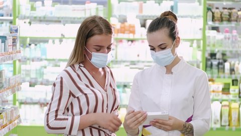 Helping clients. Horizontal view of a pharmacist helping her customer with choosing products at the local pharmacy. Both are wering protective masks. Epidemic measurements.