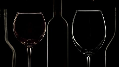 Red and white wine pouring into different wine glasses. Bottles silhouettes, low key light