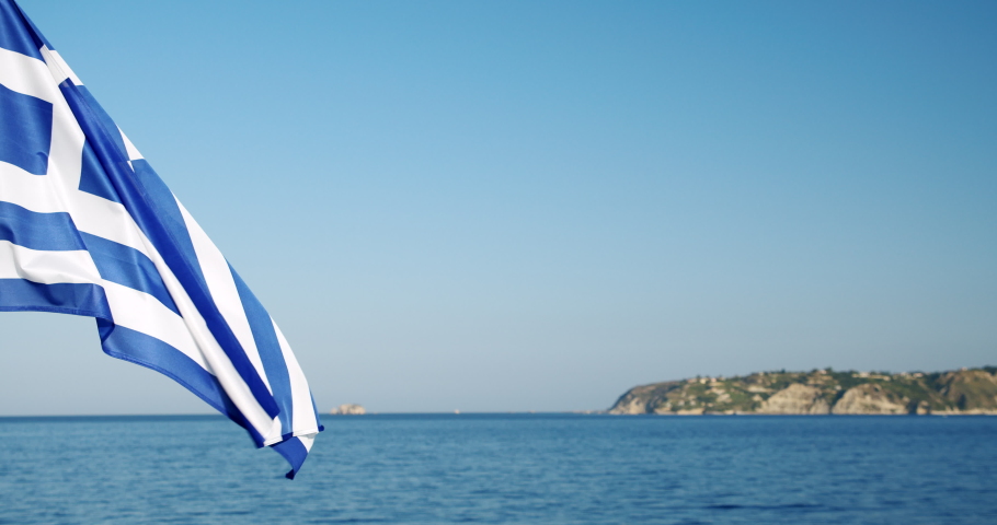 Greek flag flying on the wind flutters with sea and island in background, Greece Royalty-Free Stock Footage #1061003344