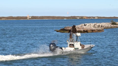 PORT ARANSAS, TX - 27 FEB 2020: Fishing boat with outboard motor and two people, enters the marina on a sunny day, floating past rocks and birds on breakwater,