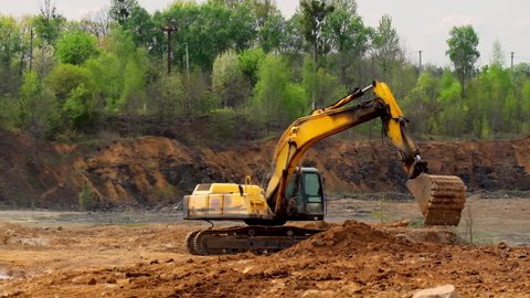 Earth moving equipment. Yellow excavator digging the ground. Excavator bucket scoops up the soil on nature background. Slow motion.